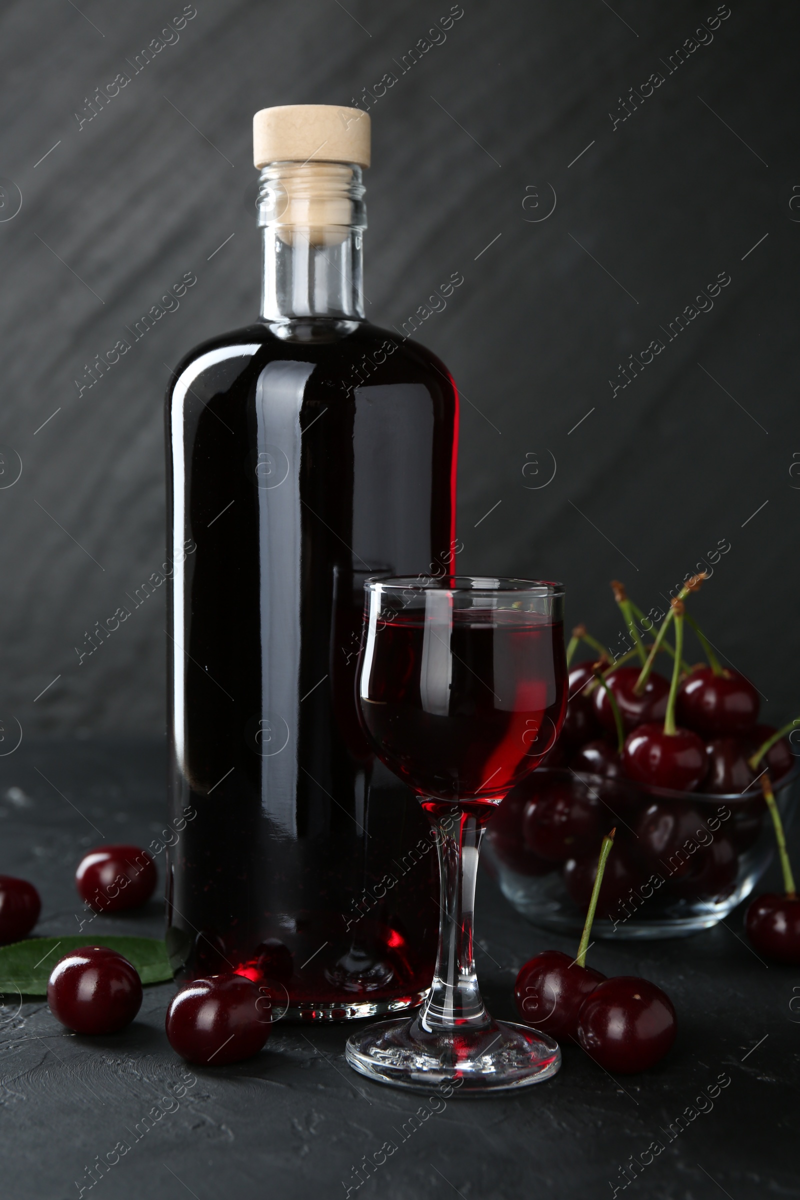 Photo of Delicious cherry liqueur and berries on black table