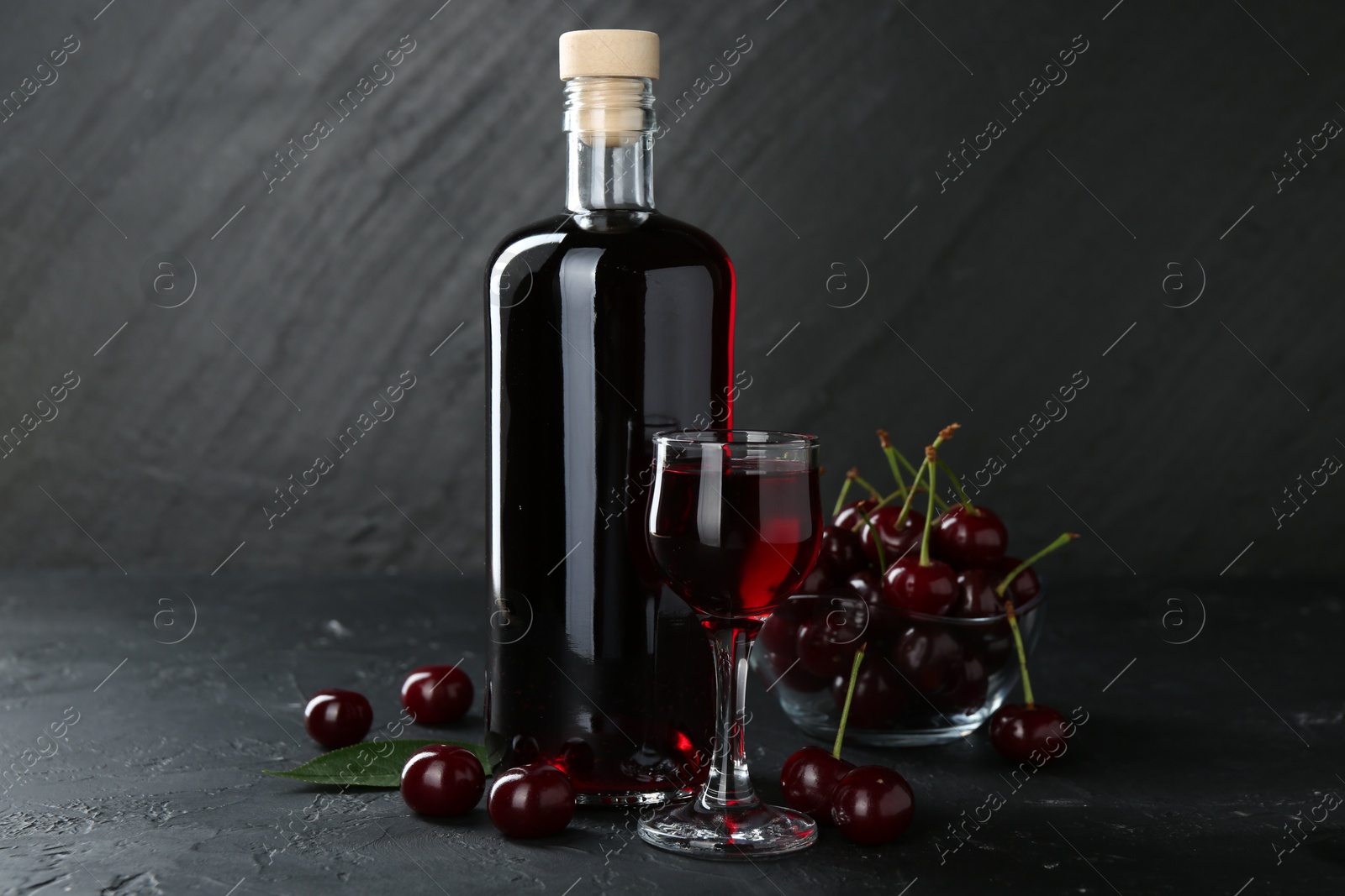 Photo of Delicious cherry liqueur and berries on black table