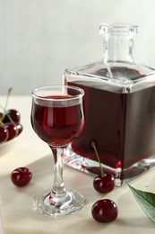 Photo of Delicious cherry liqueur and berries on white table, closeup