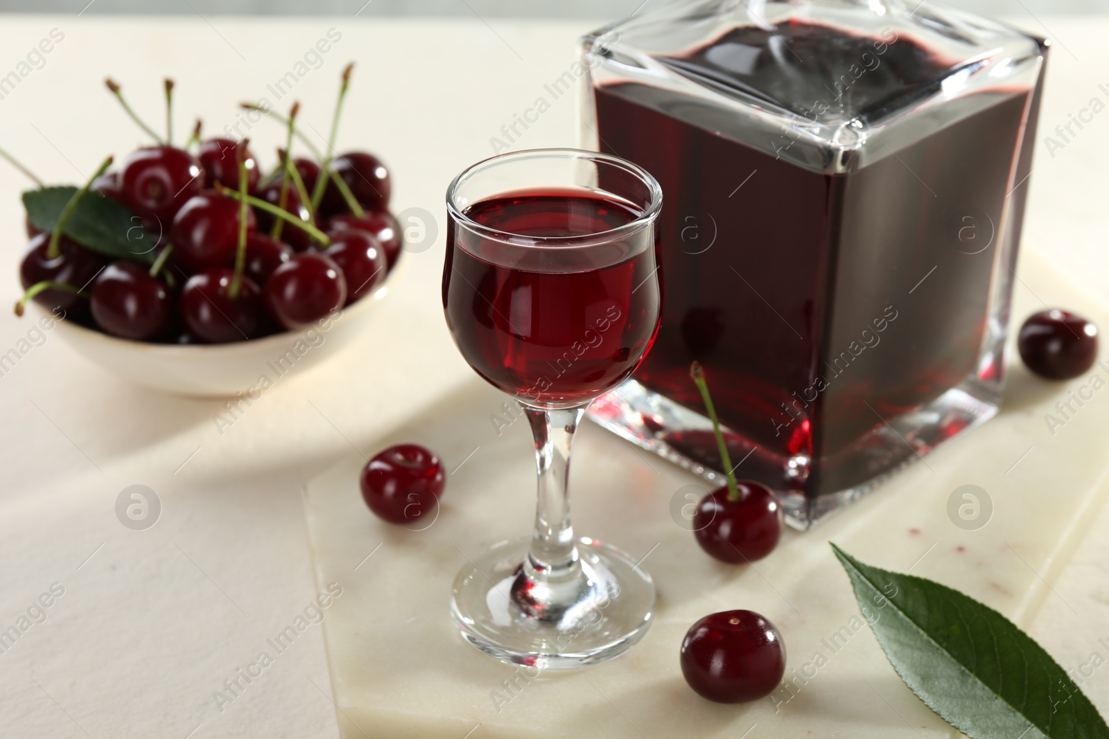 Photo of Delicious cherry liqueur and berries on white table, closeup