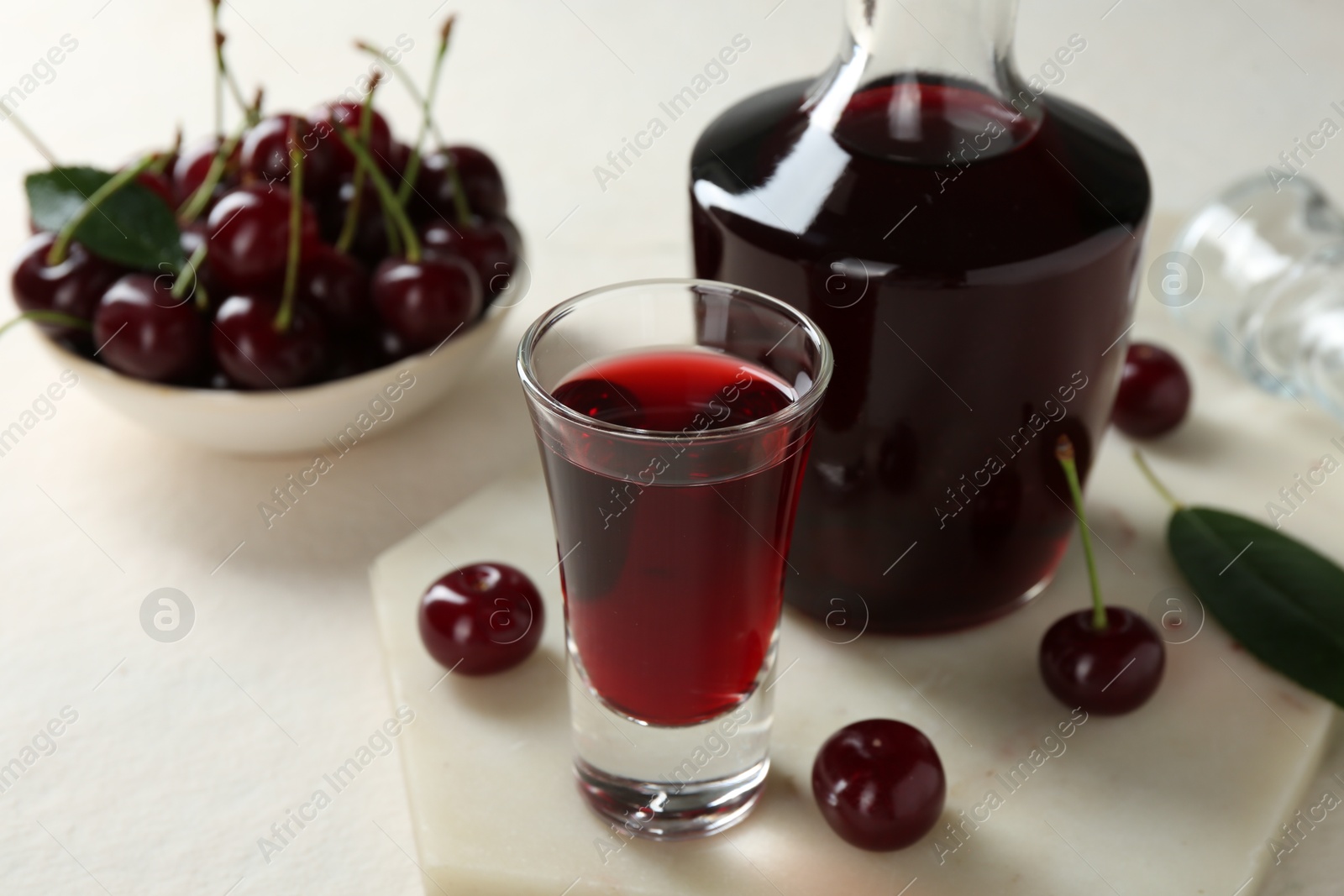 Photo of Delicious cherry liqueur and berries on white table, closeup