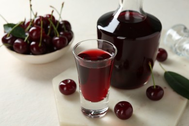 Photo of Delicious cherry liqueur and berries on white table, closeup