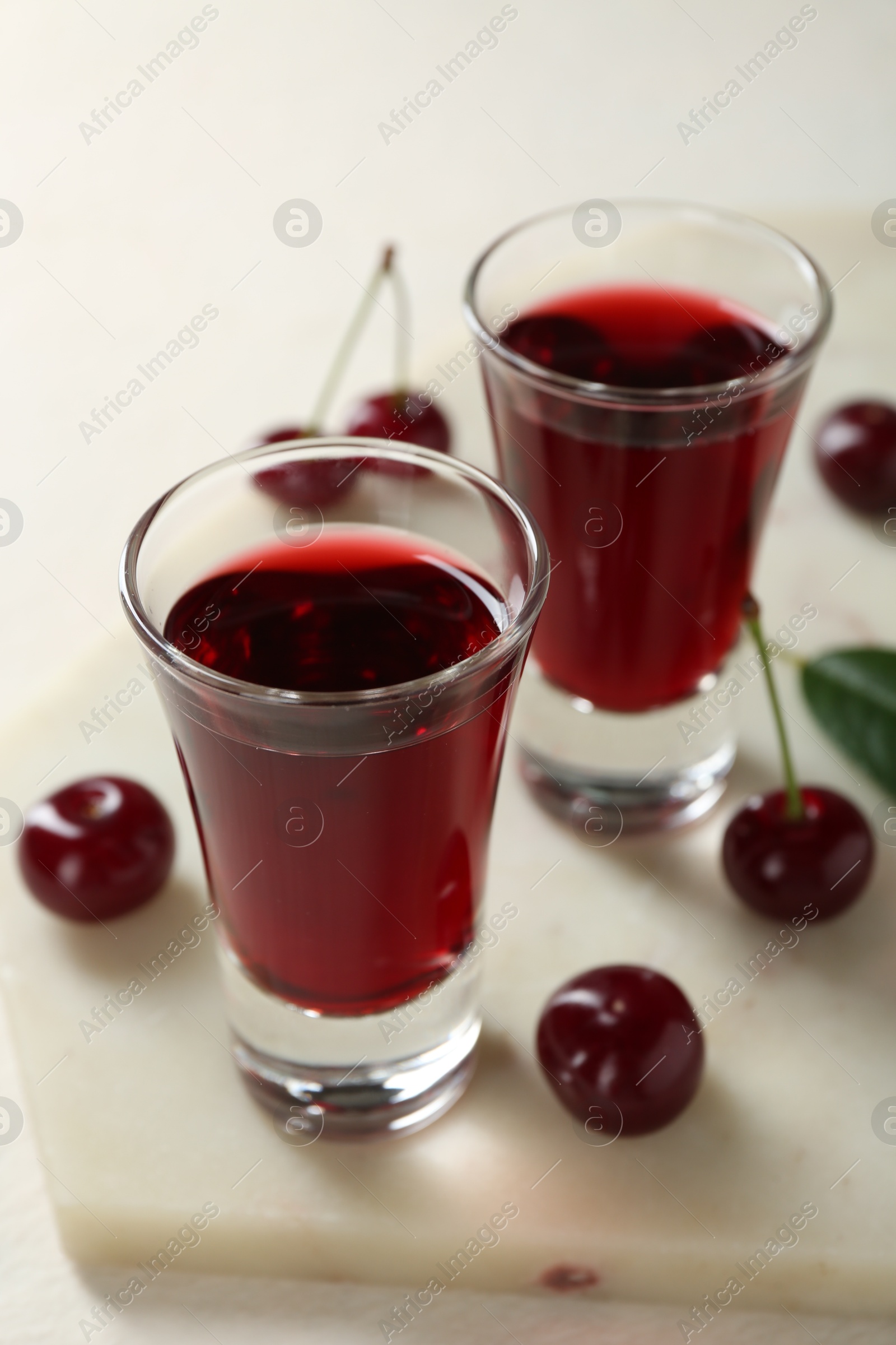 Photo of Delicious cherry liqueur in shot glasses and berries on white table, closeup