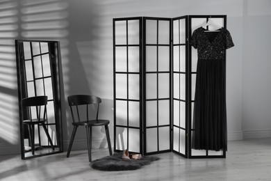 Folding screen, dress, shoes, chair and mirror near white wall indoors