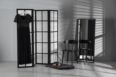 Photo of Folding screen, dress, shoes, chair and mirror near white wall indoors