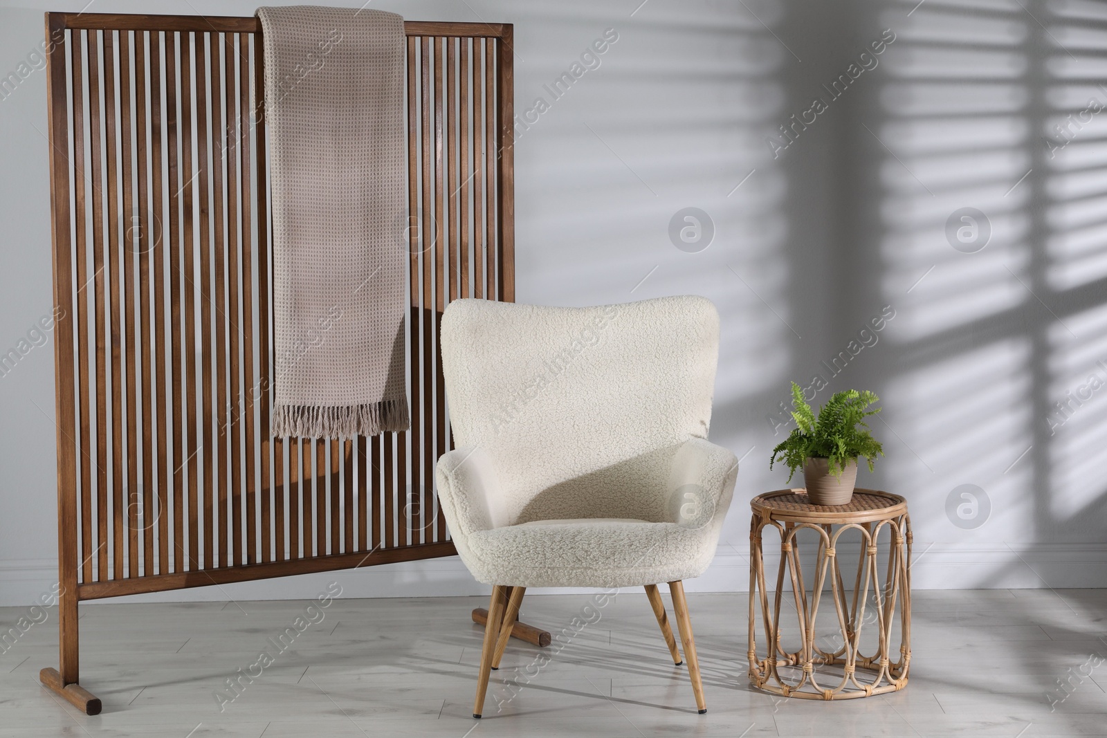 Photo of Wooden folding screen, blanket, armchair, side table and houseplant near light wall indoors