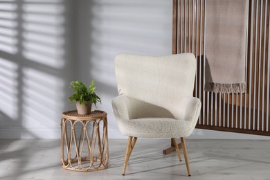 Photo of Wooden folding screen, blanket, armchair, side table and houseplant near light wall indoors