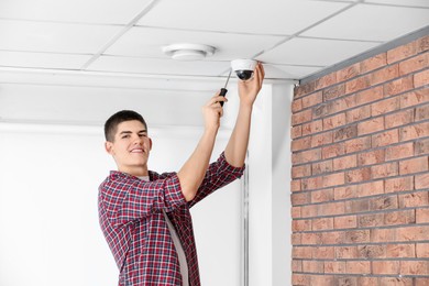 Technician with screwdriver installing CCTV camera on ceiling indoors