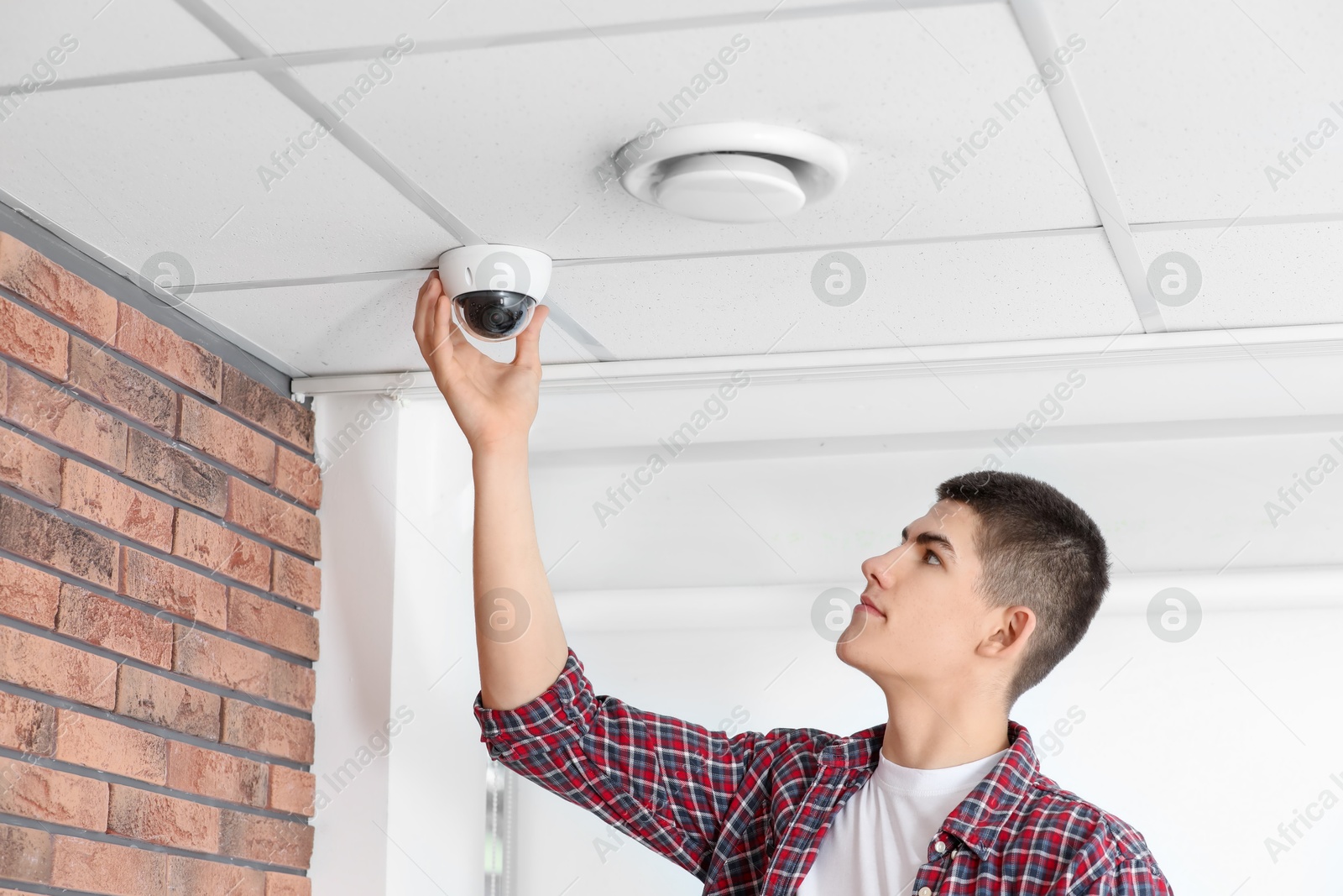 Photo of Technician installing CCTV camera on ceiling indoors