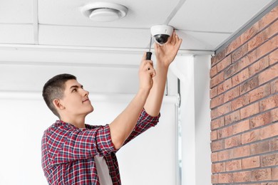 Photo of Technician with screwdriver installing CCTV camera on ceiling indoors