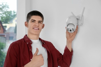 Photo of Man showing thumbs up near CCTV camera on wall indoors