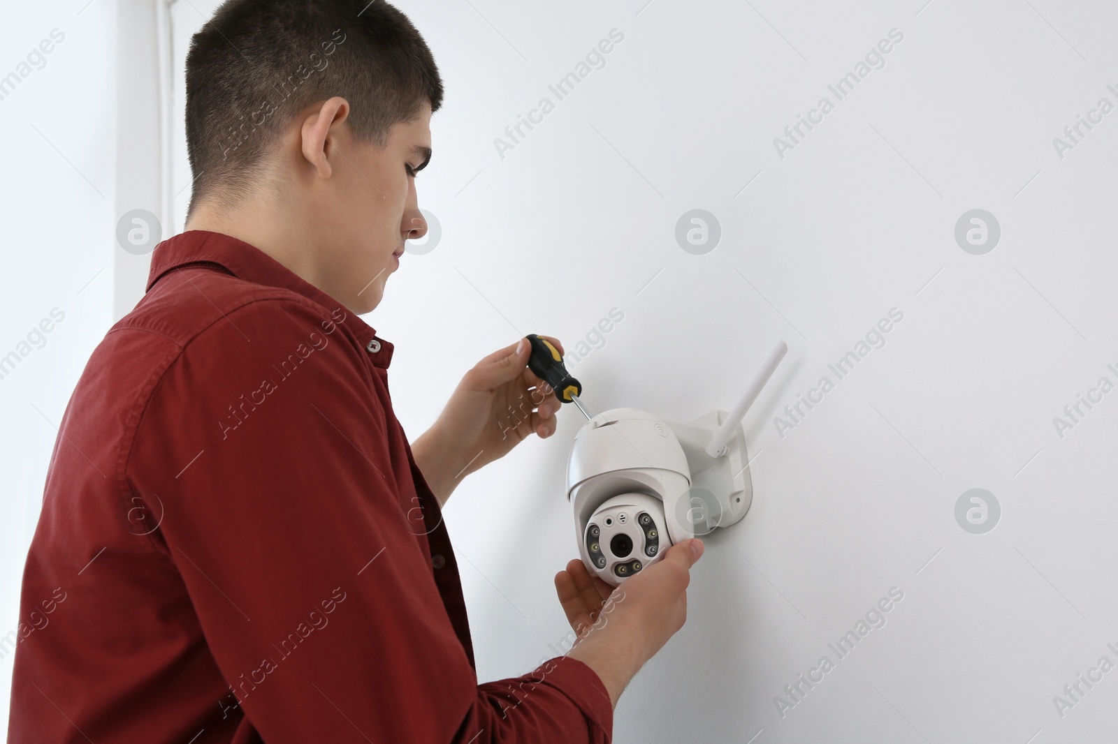 Photo of Technician with screwdriver installing CCTV camera on wall indoors, low angle view