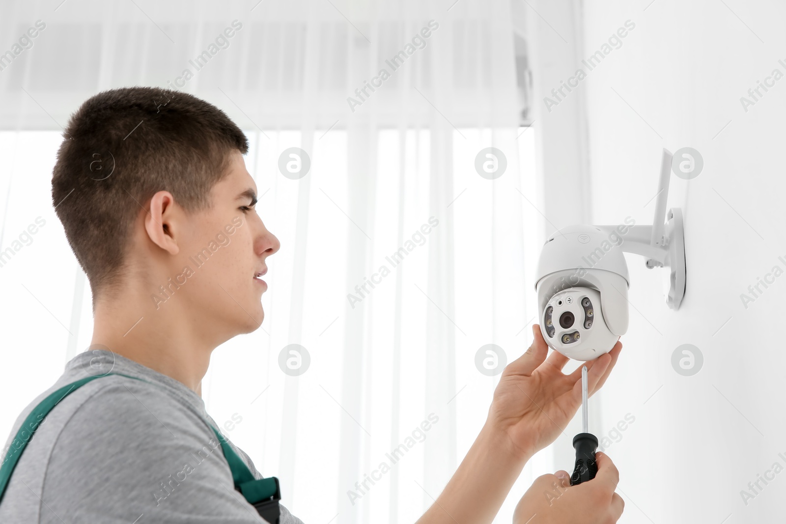 Photo of Technician with screwdriver installing CCTV camera on wall indoors