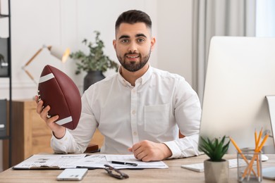 Photo of Young man with american football ball at table in office