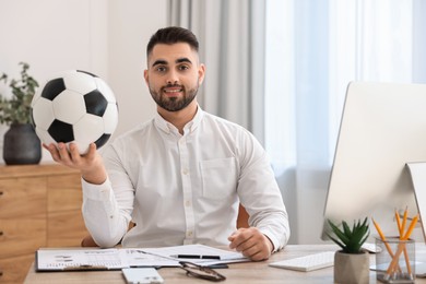 Young man with soccer ball at table in office