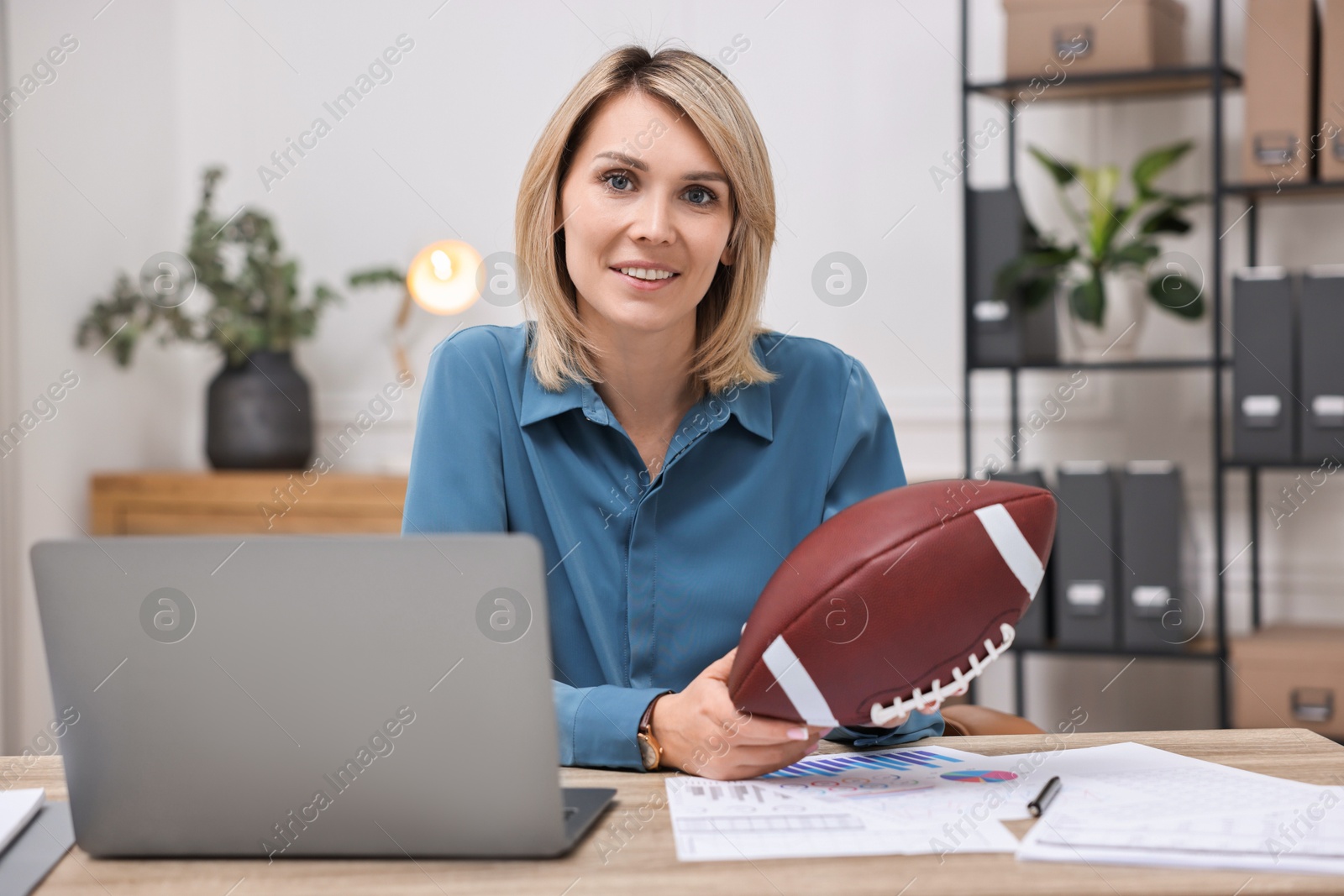 Photo of Smiling woman with american football ball at table in office