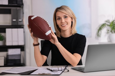 Smiling woman with american football ball at table in office