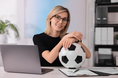 Smiling woman with soccer ball at table in office