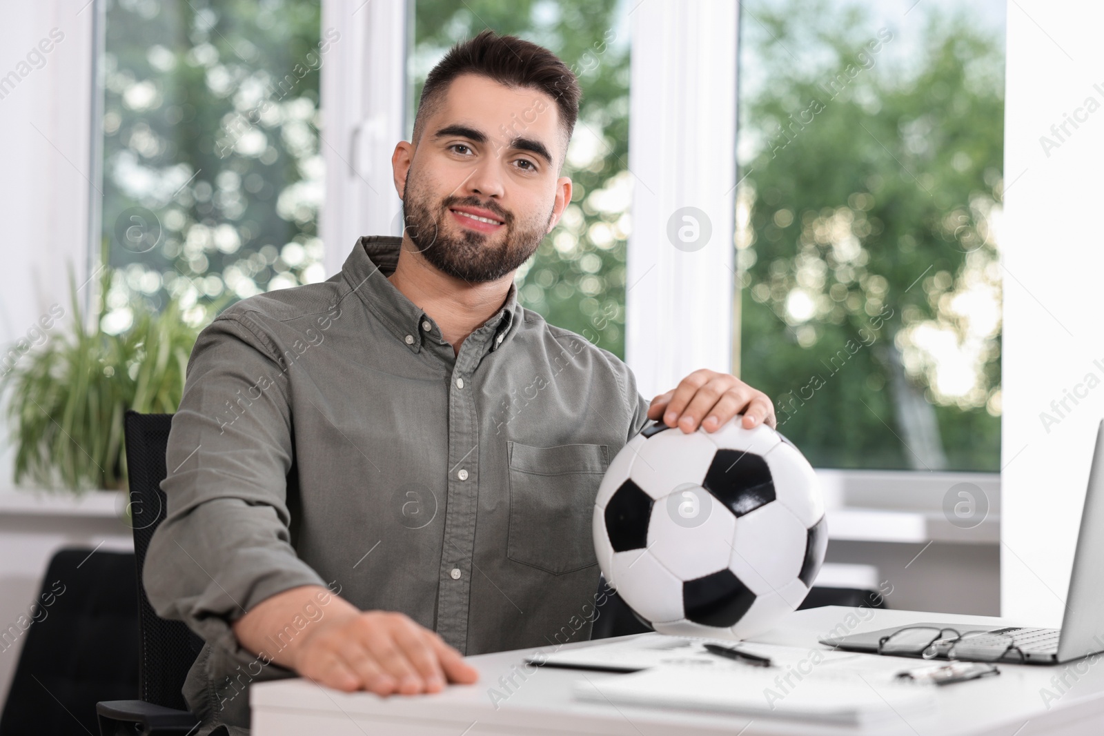 Photo of Young man with soccer ball at table in office