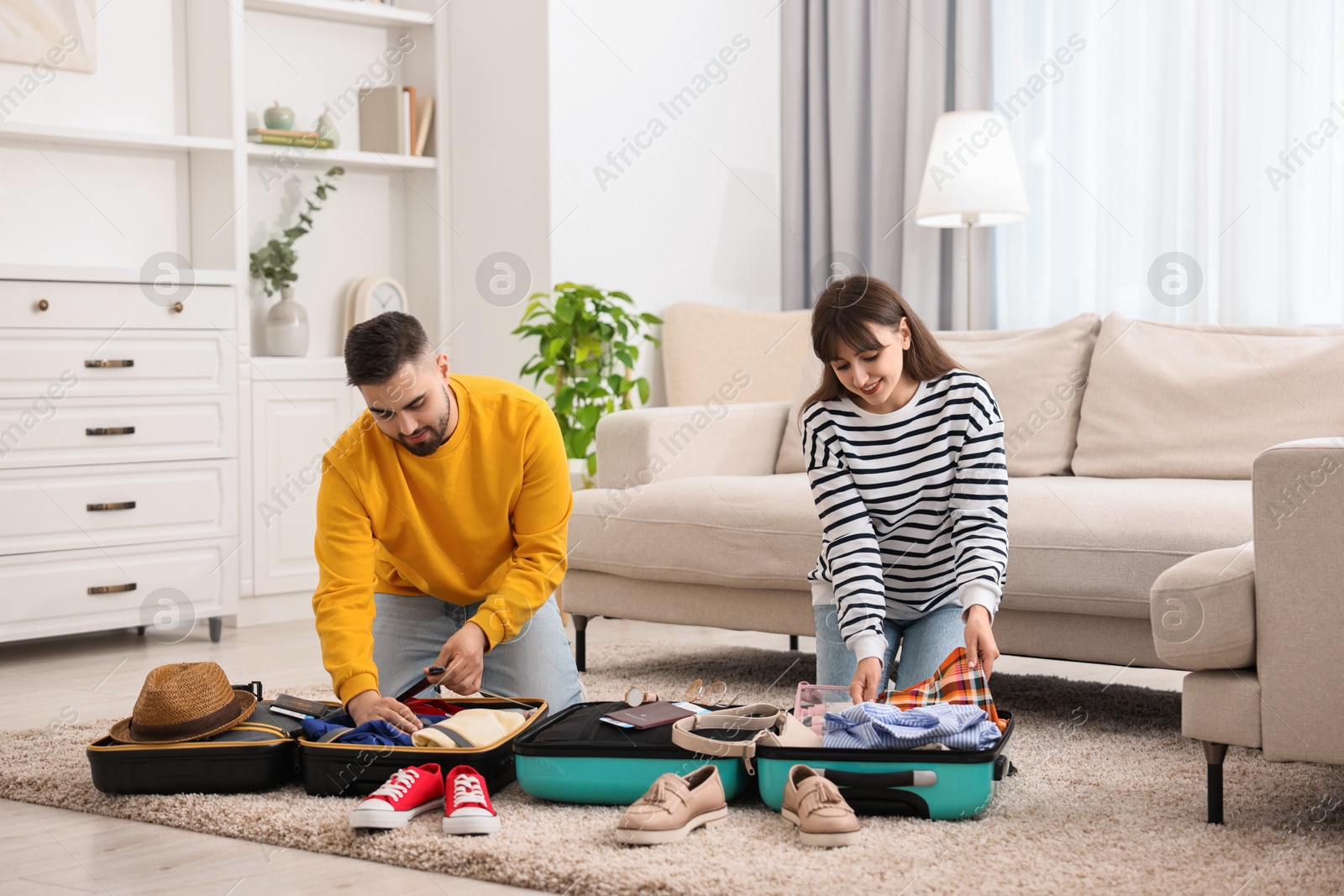 Photo of Couple packing suitcases for trip on floor at home