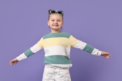 Photo of Cute little girl with sunglasses dancing on violet background