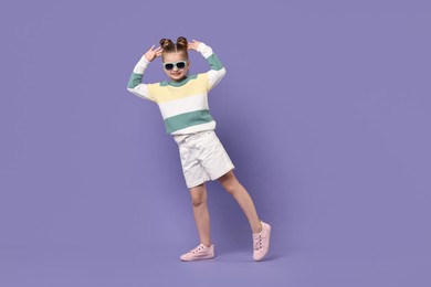 Photo of Cute little girl in sunglasses dancing on violet background