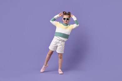 Cute little girl in sunglasses dancing on violet background
