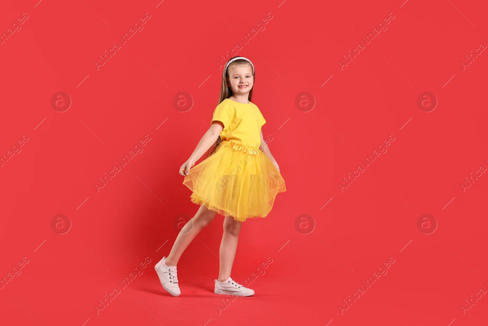 Photo of Cute little girl dancing on red background