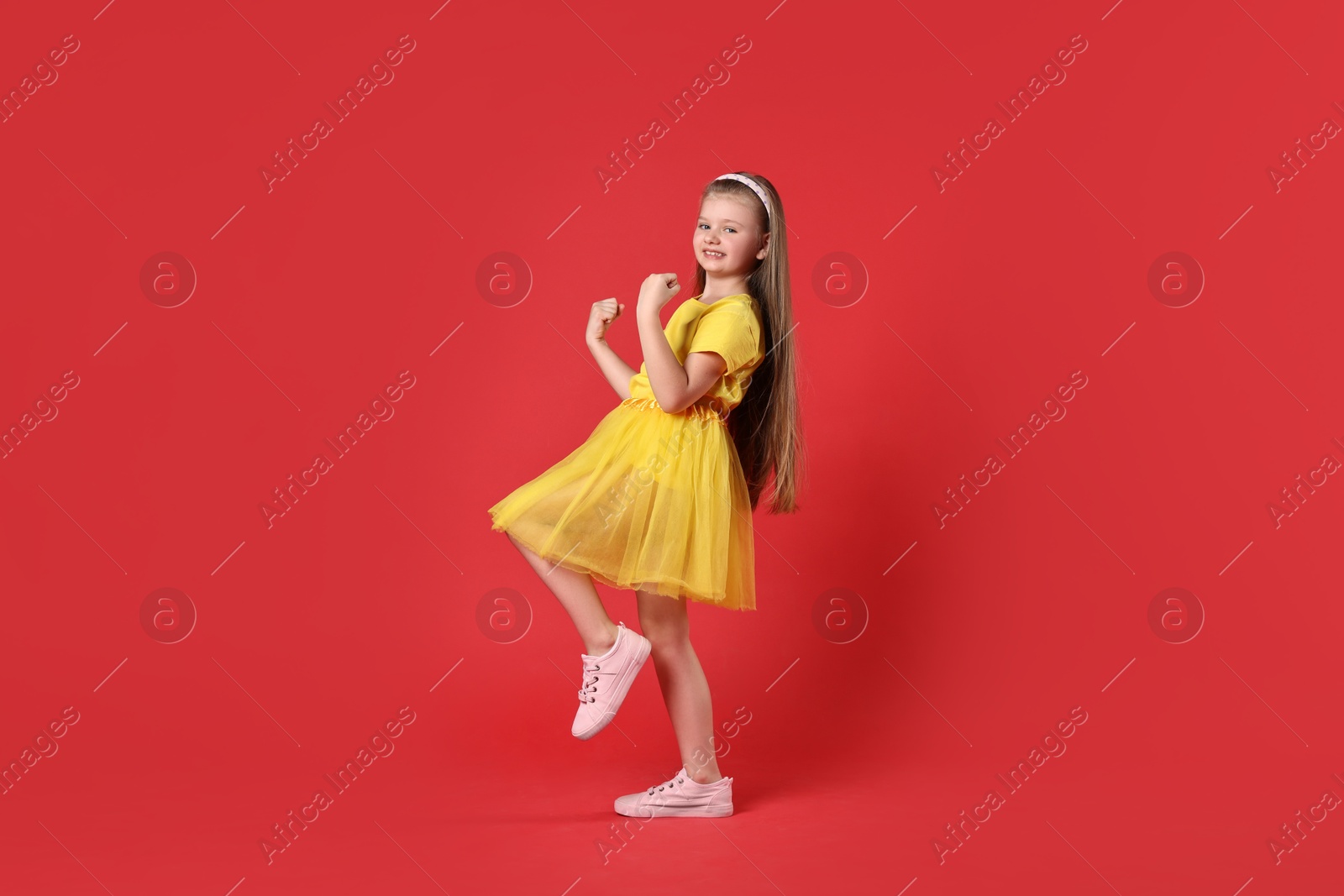 Photo of Cute little girl dancing on red background