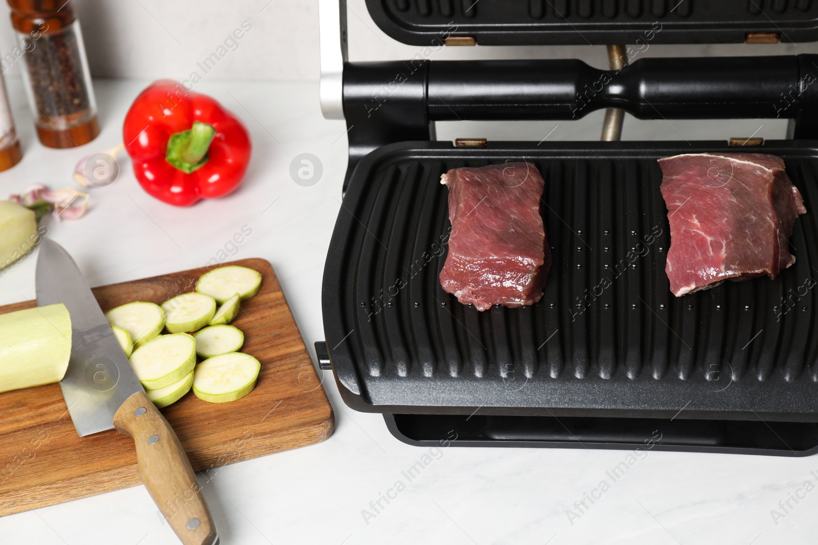 Photo of Electric grill and different products on white wooden table, closeup