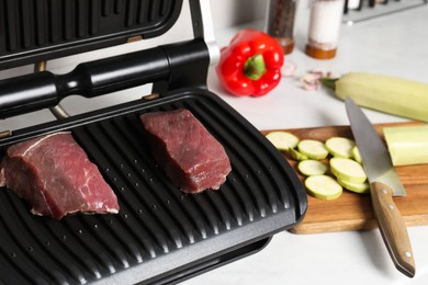 Photo of Electric grill and different products on white wooden table, closeup