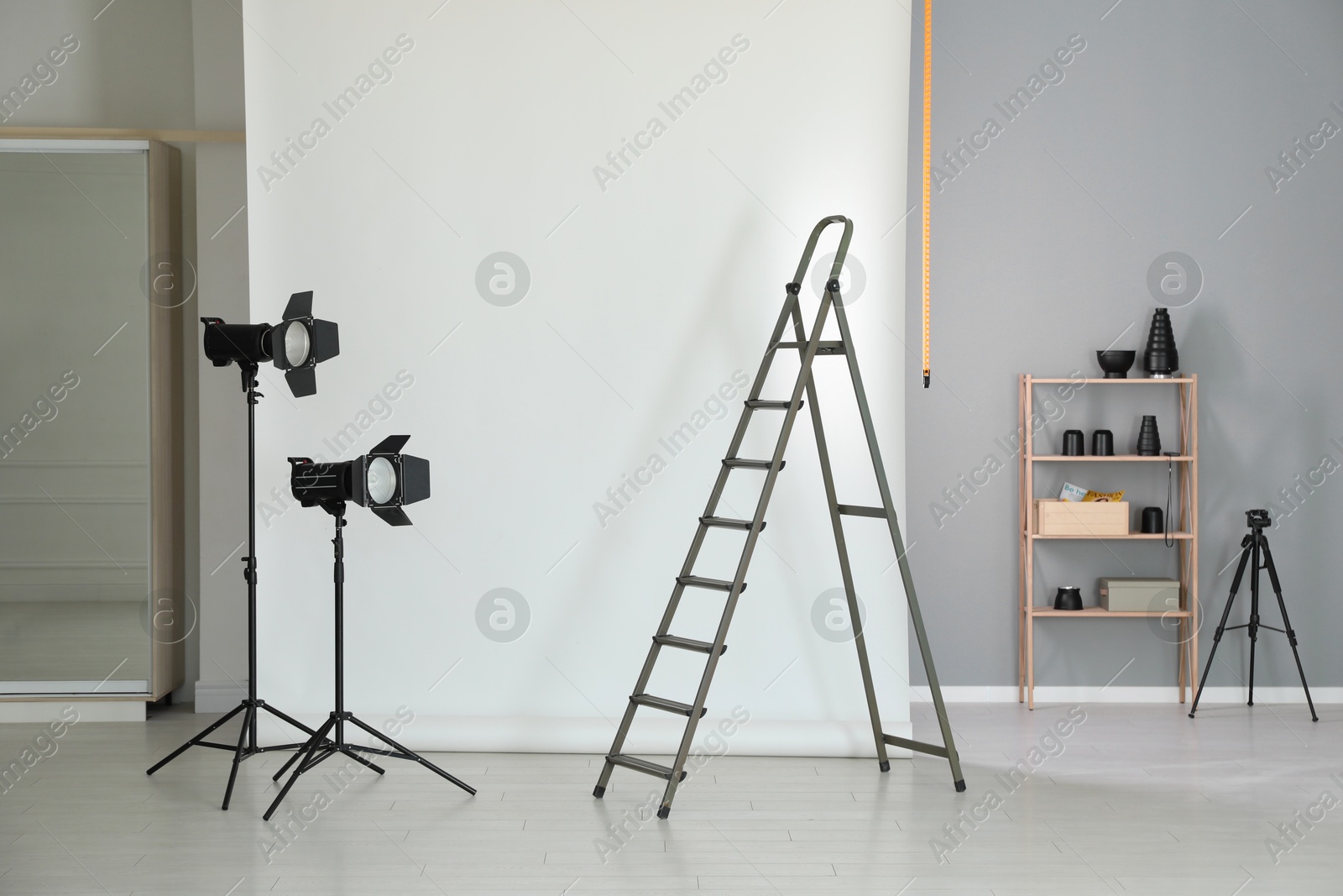 Photo of White photo background, ladder and professional lighting equipment in modern studio