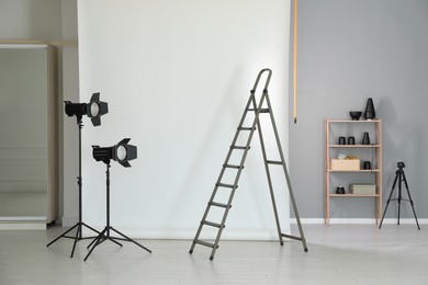 Photo of White photo background, ladder and professional lighting equipment in modern studio