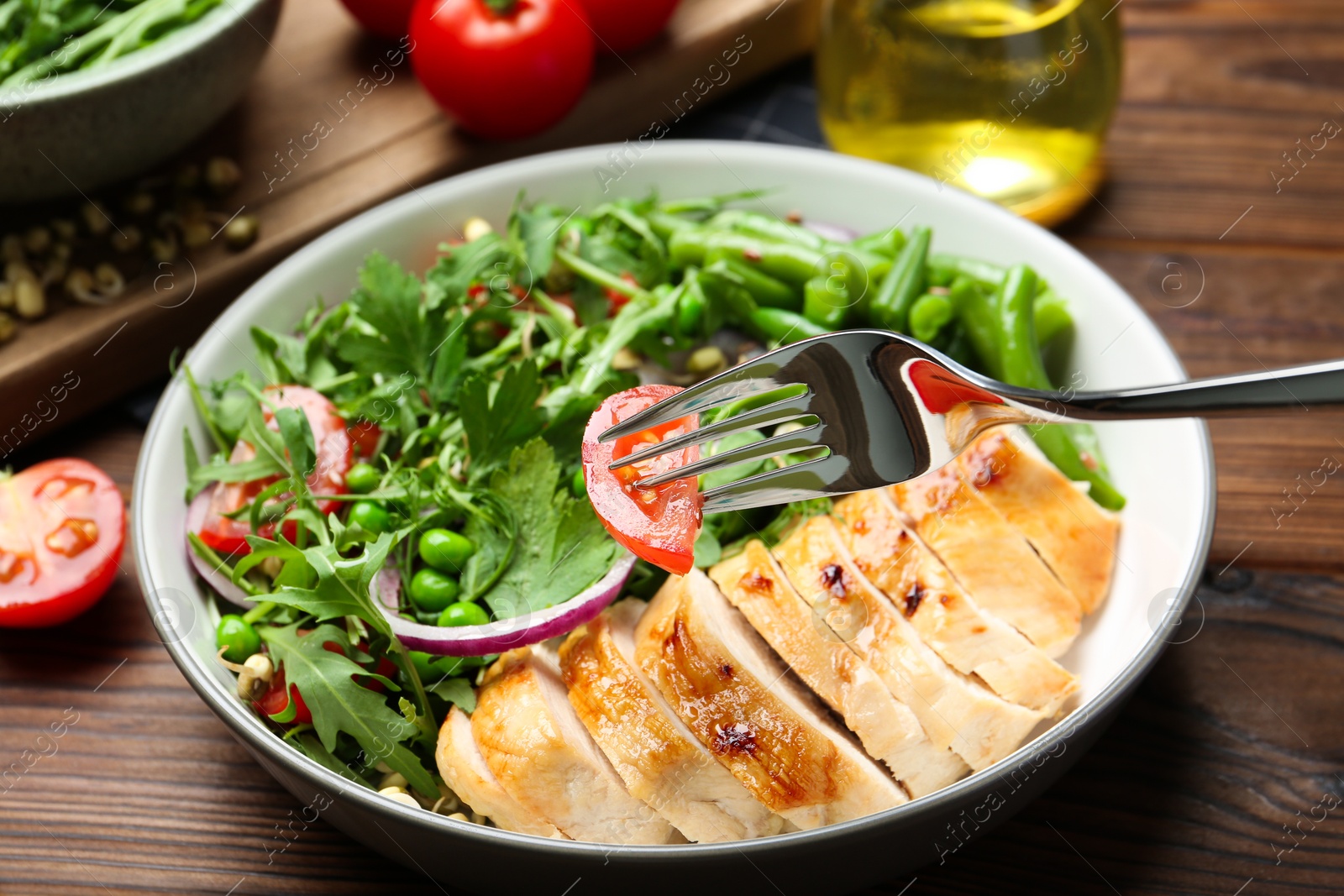 Photo of Healthy meal. Eating tasty salad and chicken breast with fork from bowl on wooden table, closeup