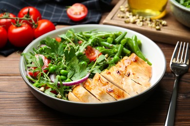 Healthy meal. Tasty salad and chicken breast in bowl on wooden table, closeup