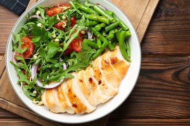 Photo of Healthy meal. Tasty salad and chicken breast in bowl on wooden table, top view