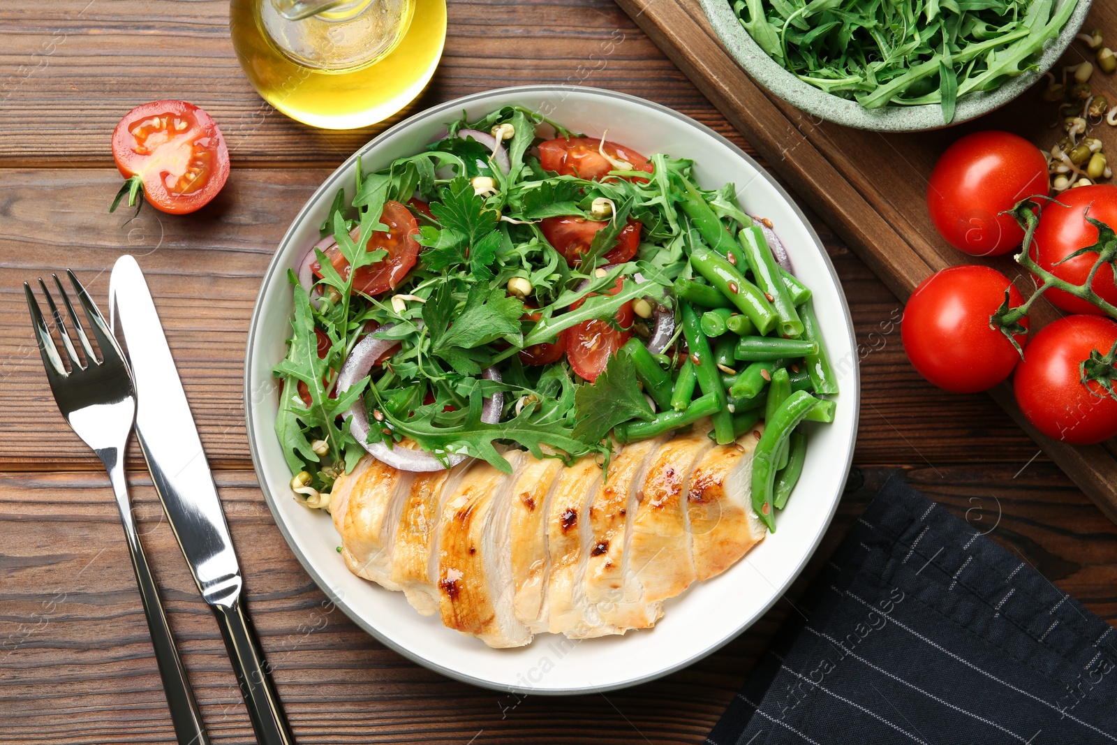 Photo of Healthy meal. Tasty salad and chicken breast in bowl and cutlery on wooden table, flat lay