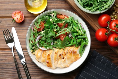 Photo of Healthy meal. Tasty salad and chicken breast in bowl and cutlery on wooden table, flat lay