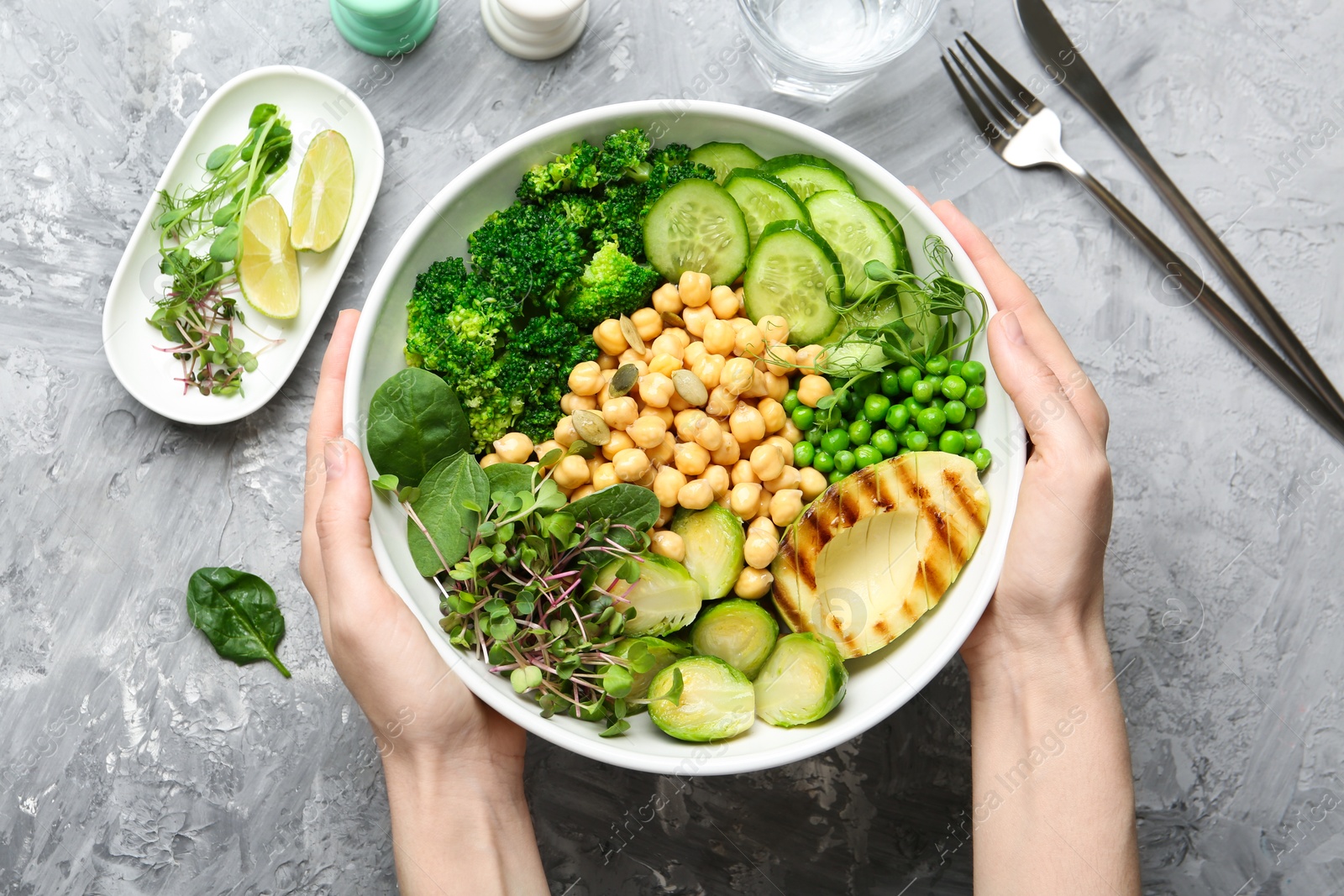 Photo of Healthy meal. Woman with bowl of tasty vegetables and chickpeas at grey table, top view