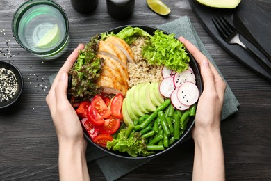 Photo of Healthy meal. Woman with bowl of tasty products at black wooden table, top view