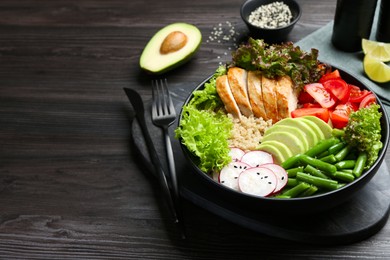 Photo of Healthy meal. Tasty products in bowl and cutlery on black wooden table, space for text