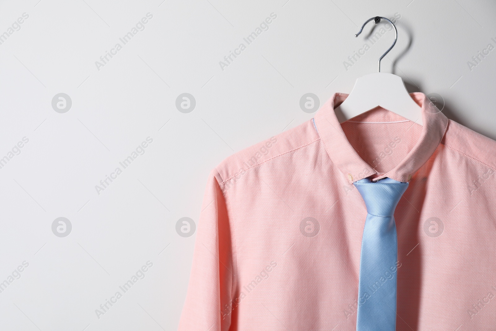 Photo of Hanger with shirt and necktie on light wall, space for text