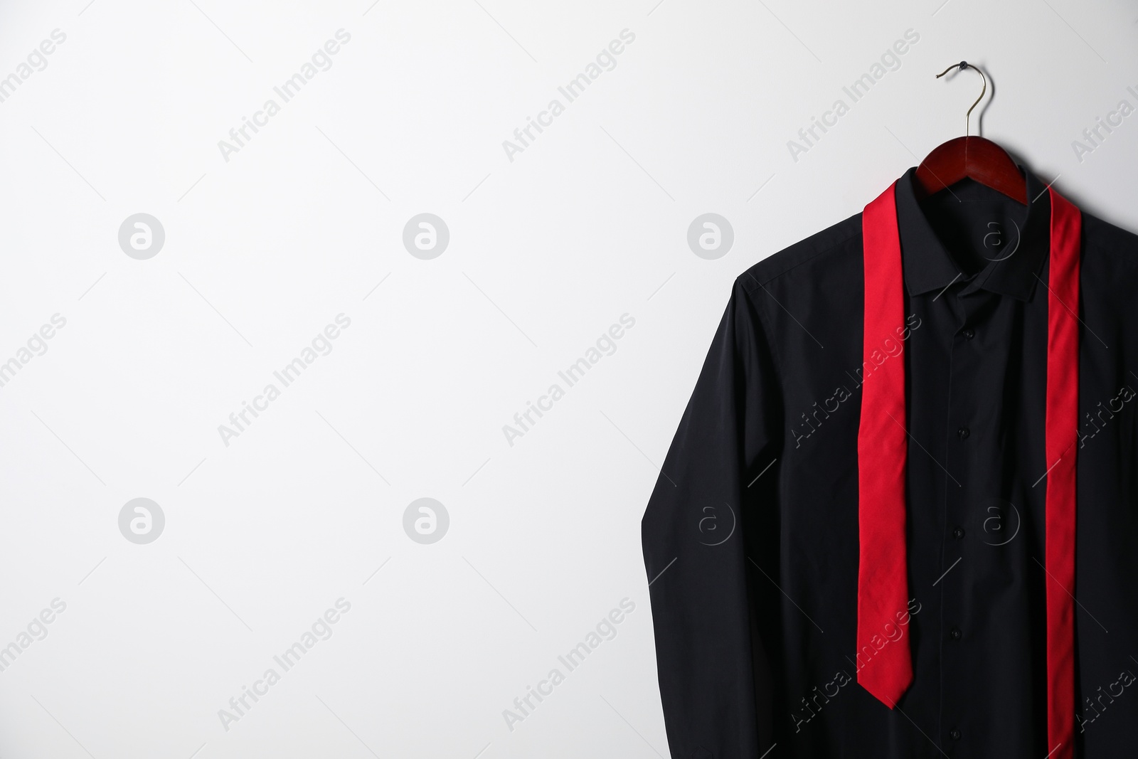 Photo of Hanger with black shirt and necktie on light wall, space for text