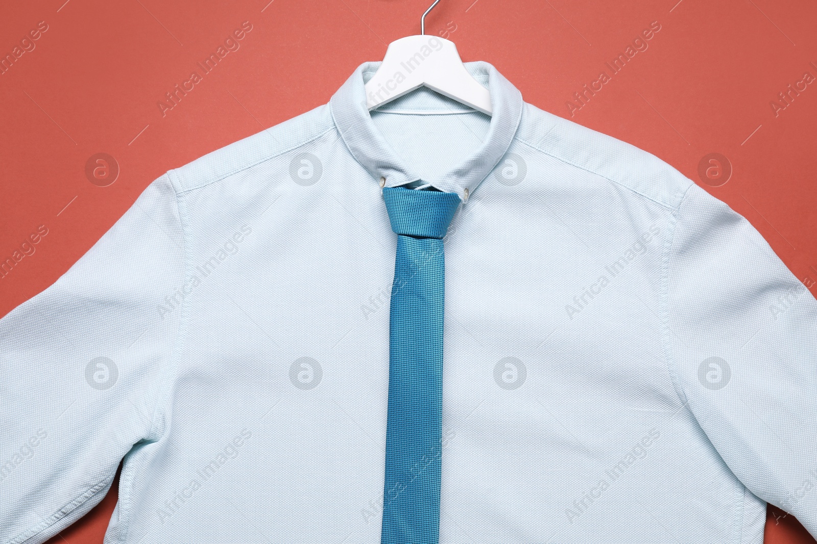 Photo of Hanger with white shirt and turquoise necktie on coral background, top view