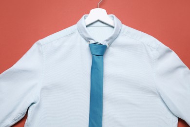 Photo of Hanger with white shirt and turquoise necktie on coral background, top view