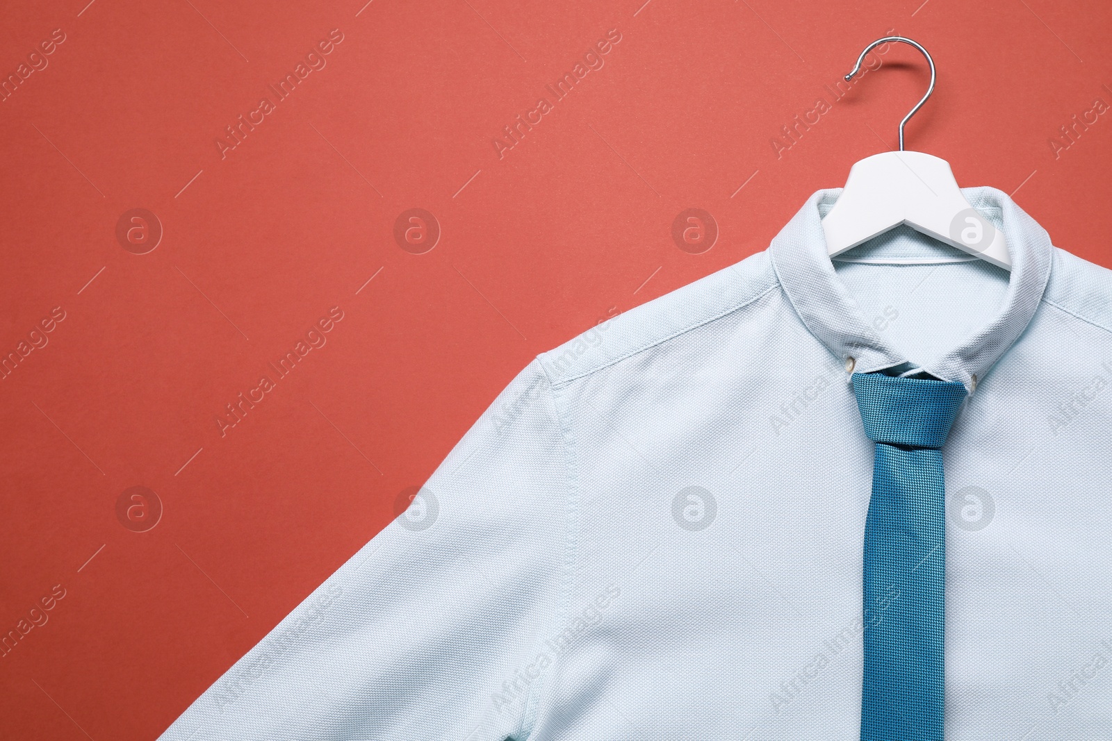 Photo of Hanger with white shirt and turquoise necktie on coral background, top view. Space for text