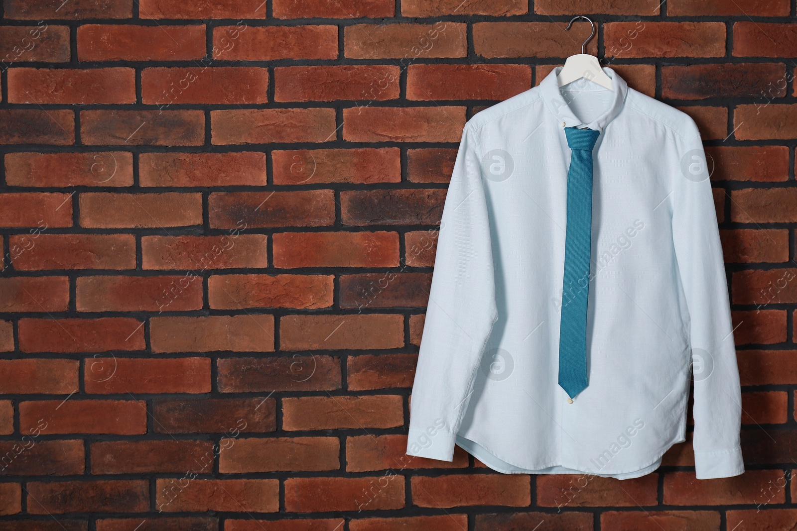 Photo of Hanger with white shirt and turquoise necktie on red brick wall, space for text