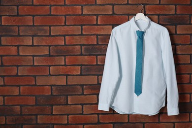 Hanger with white shirt and turquoise necktie on red brick wall, space for text