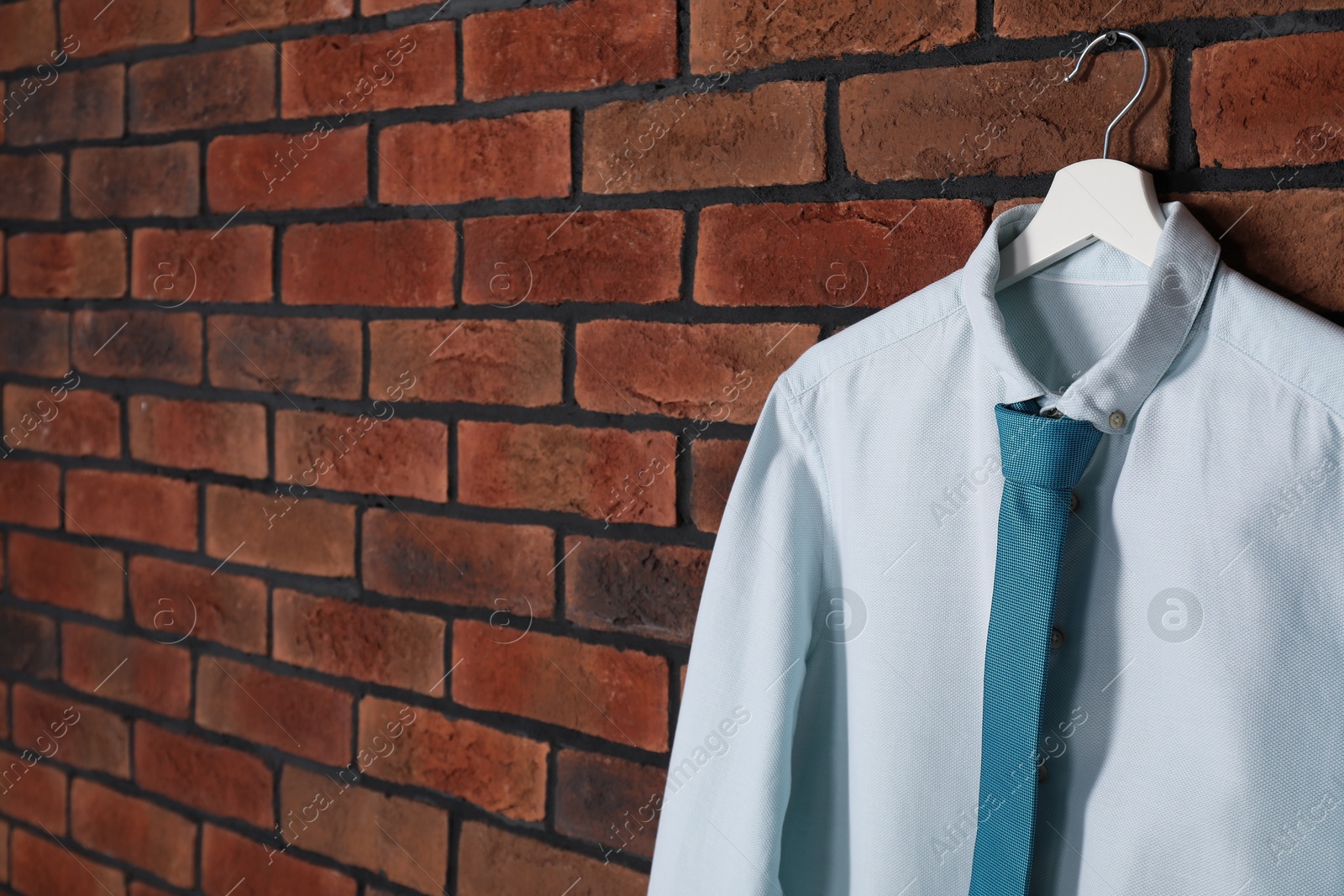 Photo of Hanger with white shirt and turquoise necktie on red brick wall, space for text