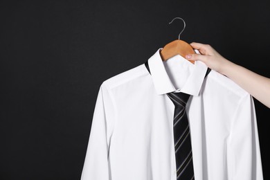 Woman holding hanger with white shirt and necktie on black background, space for text